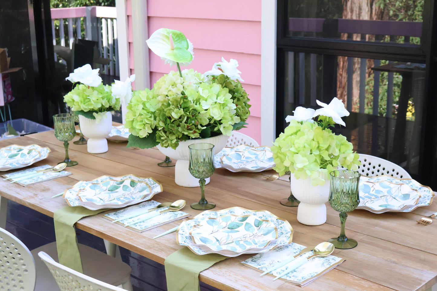 Dining table set with green floral centerpieces, white plates, and glasses on a wooden deck.